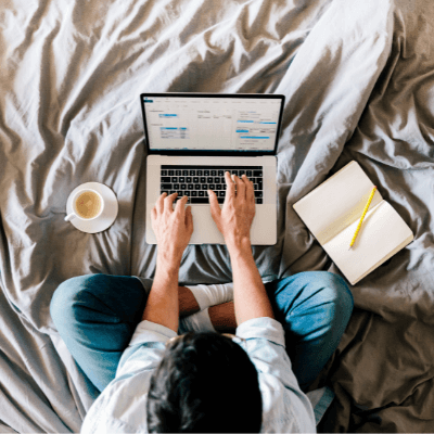 Overhead view of a man working on a laptop from his bed at home